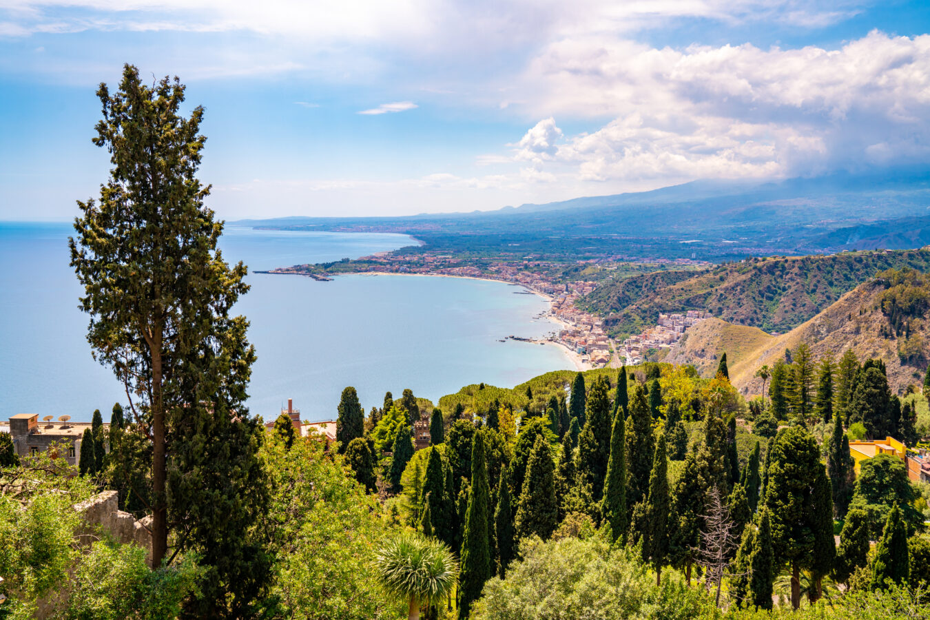 An aerial shot of Taormina Sicily, showcasing the greenery and the coast.